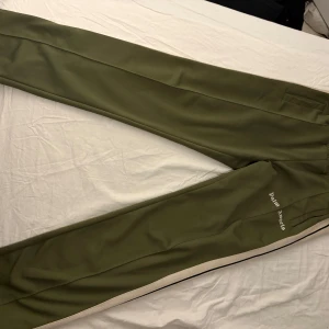 Gröna byxor från Palm Angels - Snygga gröna byxor från Palm Angels med vita sidoremsor. Perfekta för en avslappnad stil med en touch av lyx. Byxorna har en modern passform och är tillverkade i ett bekvämt material.