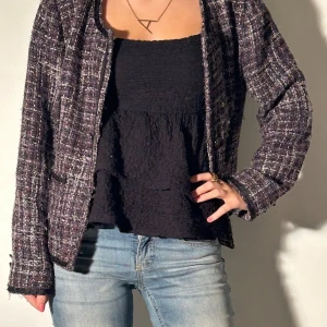 Rutig kavaj i tweed - Snygg rutig kavaj i tweed med en klassisk look. Den har långa ärmar och en öppen design utan knappar. Perfekt för en stilren och chic outfit.