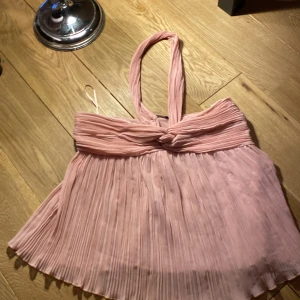 Rosa plisserad topp från Zara - Säljer en söt rosa plisserad topp från Zara med knytband i halsen. Perfekt för sommarens varma dagar. Toppen har en luftig och elegant design.