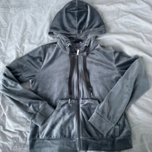 Grå hoodie från Gina Tricot - Mysig grå hoodie från Gina Tricot med dragkedja och huva. Tillverkad i mjukt material med långa ärmar och praktiska fickor framtill. Perfekt för en avslappnad stil.