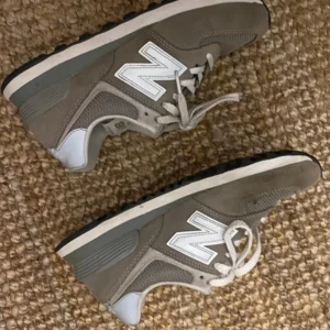 Grå sneakers från New Balance - Snygga grå sneakers från New Balance med vit logga och snörning. Skorna har en bekväm passform och är perfekta för vardagsbruk. De har en kombination av mocka och meshmaterial för en stilren look.