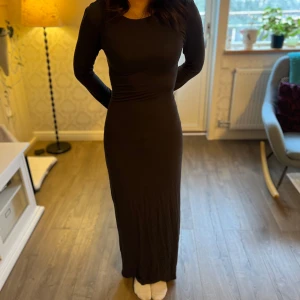 Svart långklänning - Elegant svart långklänning med långärmad design. Klänningen har en figurnära passform som framhäver silhuetten. Perfekt för en stilren och sofistikerad look.