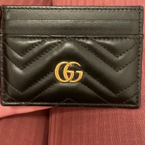 Svart quiltad kortfodral från Gucci - Snyggt svart kortfodral från Gucci i skinn med quiltad design och guldiga GG-detaljer. Perfekt för att hålla dina kort organiserade med stil.