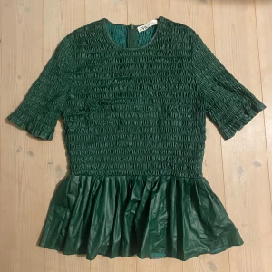 Grön topp med volang från Zara - Säljer en snygg grön topp från Zara med trekvartsärm och volangdetalj i nederkant. Toppen har en smockad struktur och en dragkedja i ryggen för enkel påklädning. Perfekt för att ge en stilfull touch till din outfit.