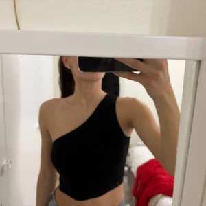 Svart oneshoulder topp från NA-KD - Snygg svart oneshoulder topp från NA-KD i storlek XS. Perfekt för en stilren look med en asymmetrisk design. Tillverkad i ett mjukt och bekvämt material.