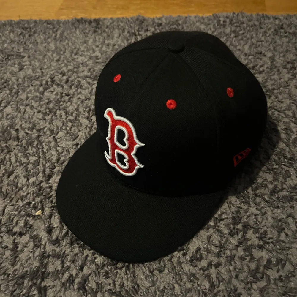 Snygg svart keps från New Era med röd broderad 'B' logga framtill och MLB-logga baktill. Under skärmen står det 'BOSTON' i rött. Perfekt för sommaren , full fitted storleken är 57,7 men tror den har krympt lite. Asusteet.