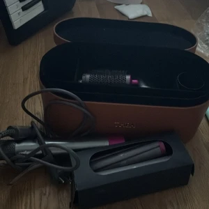 DYSON med olika tillbehör - OBS lånad bild och kan gå ner i pris vid snabb affär. En svart och rosa dyson med alla delar tillkommer. I princip oanvänd. En låda att ha allt i i brunt som har ingraverat ”Thea”. Barrels är i long så fungerar att locka långt hår💕 skriv för  bilder