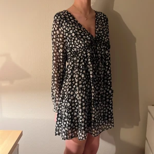 Svart blommig klänning - Charmig svart klänning med vita blommor och v-ringad design. Den har långa ärmar och en luftig passform som ger en bekväm känsla. Perfekt för en avslappnad stil. Från HM. priset kan diskuteras! Använd fåtal gånger❤️