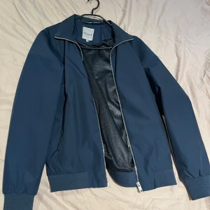 Mörkblå bomberjacka från Elvine - Snygg mörkblå bomberjacka från Elvine med dragkedja framtill. Jackan har ribbade muddar vid ärmslut och nederkant samt en klassisk krage. Perfekt för en stilren look.