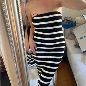 Randig axelbandslös klänning - Snygg axelbandslös klänning med svartvita ränder. Den har en tight passform och är perfekt för en stilren look. Klänningen är ribbad och sträcker sig ner till knäna. Storlek S med lapp kvar 