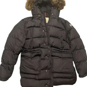 Moncler Senega - Säljer en svart dunjacka från Moncler. Jackan har långa ärmar och flera praktiska fickor med knappar. Perfekt för kalla vinterdagar.