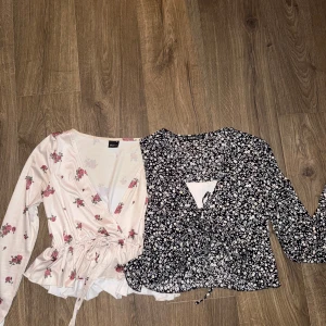 Två omlottblusar med blommönster - Säljer två fina omlottblusar. Den ena är vit med rosa blommor och har långa ärmar och knytning i midjan. Den andra är svart med vita blommor med knytning. 