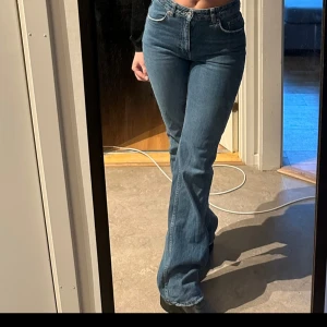 Blå bootcut jeans - Snygga blå bootcut jeans med hög midja. Perfekta för en avslappnad stil med en touch av retro. De har en klassisk femficksdesign och stängs med dragkedja och knapp.