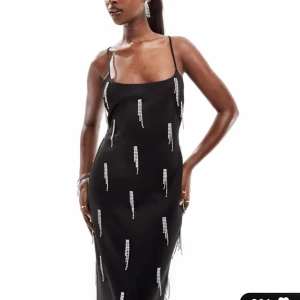 Svart långklänning med strassdetaljer - Elegant svart långklänning med smala axelband och öppen rygg. Klänningen har glittriga strassdetaljer som ger en lyxig känsla. Perfekt för en glamorös kväll.