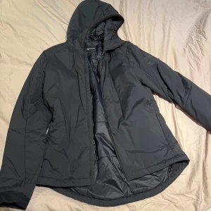 Svart vindjacka med huva - Snygg svart vinterjacka med huva och dragkedja framtill. Perfekt för blåsiga dagar och har en stilren design. Jackan är långärmad och har en bekväm passform.