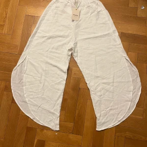 Vita byxor från Pull&Bear - Unika vita byxor från Pull&Bear med en luftig och vid design. Byxorna har en elastisk midja för extra komfort och är tillverkade i ett lätt material, perfekt för varma dagar.