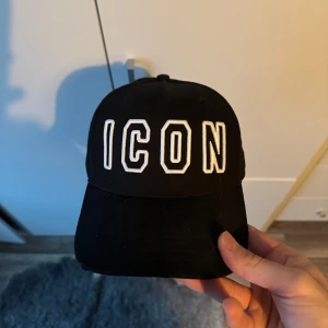Svart keps från Dsquared2 - Snygg svart keps från Dsquared2 med texten 'ICON' broderad framtill i vitt. Baktill finns justerbart spänne och Dsquared2-logga. Perfekt för en stilren look. Använd max 5 gånger, köpt helt ny.