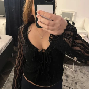 Svart spetsblus från Pieces - Säljer en elegant svart spetsblus från Pieces, köpt på Only. Blusen har långa ärmar och en v-ringad design med knytning framtill. Perfekt för en stilfull look.  