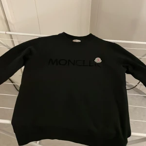 Svart tröja från Moncler - Säljer en stilren svart tröja från Moncler med deras logotyp broderad på bröstet. Tröjan har långa ärmar och en klassisk passform. Perfekt för en avslappnad och trendig look.