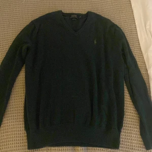 Mörkgrön tröja från Polo Ralph Lauren - Säljer en stilren mörkgrön tröja från Polo Ralph Lauren i bomull. Tröjan har en v-ringad design och långa ärmar, perfekt för en klassisk look. Den är tillverkad i mjukt material för extra komfort.