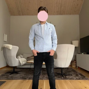 Ralph Lauren skjorta  - Snygg ljusblå och vit randig skjorta med en liten broderad logga på bröstet. Skjortan har långa ärmar och en klassisk krage, perfekt för en stilren look. Passar bra till både jeans och chinos. Jag på bilden är 172