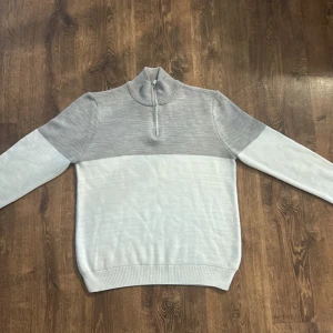 Grå och vit tröja med dragkedja från Studio - Snygg grå och vit tröja från Studio med dragkedja vid halsen. Tröjan har en ribbad krage och är långärmad, perfekt för kyligare dagar. Den är stilren och enkel att matcha med olika outfits.