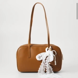 Brun axelväska med spetsdetalj - Snygg brun axelväska i syntetmaterial. Väskan har en praktisk dragkedja och långa remmar för bekväm användning. Detaljerna går att ta bort. Helt ny🤎