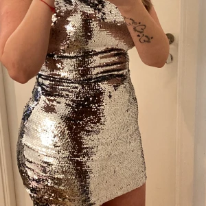 Silver paljettklänning - Snygg och glittrig silverfärgad klänning täckt med paljetter. Perfekt för att sticka ut på festen. Klänningen har en tight passform och är ärmlös, vilket ger en elegant look. Den korta längden gör den extra festlig. Perfekt för nyår eller andra speciella tillfällen. ✨