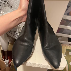 Svarta stövletter i skinn - Snygga svarta stövletter i skinn med spetsig tå och klack. Tillverkade i Italien, dessa boots har en elegant design som passar perfekt för en stilren look.