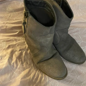 Grå boots med dragkedja - Snygga grå boots med dragkedja på sidan och en stabil klack. Perfekta för både vardag och lite finare tillfällen. De har en rundad tå och en diskret glittrig yta som ger en extra touch.