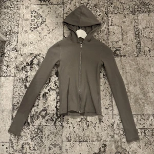 Grå kofta med dragkedja och huva - Säljer en stilren grå hoodie med dragkedja och huva. Den har en tight passform och långa ärmar, perfekt för en casual look. Materialet är mjukt och bekvämt. 