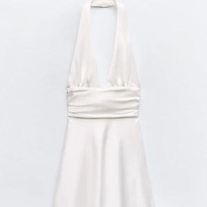 Vit halterneck klänning - Sjukt fin och elegant halterneck klänning med djup urringning och en rosett i ryggen, perfekt till sommaren, student eller skolavslutning. Kläningen är i satin och i helt nyskick, prislappen sitter fortfarande kvar då den inte blivit andvänd. Säljer då jag hittade en annan student klänning❤️