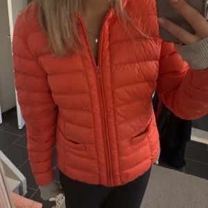 Rosa pufferjacka från Holly & Whyte - Säljer en snygg och trendig orange/rosa tunn pufferjacka från Holly & Whyte. Jackan har en dragkedja framtill och långa ärmar. Perfekt för kyligare vårdagar med sin quiltade design. En stilren och praktisk jacka för alla tillfällen.