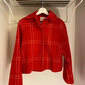 Röd rutig jacka från NA-KD - Snygg röd rutig jacka från NA-KD med knappar framtill. Jackan har en croppad passform och långa ärmar. Den är tillverkad i ett mjukt material som känns bekvämt att bära.