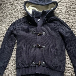 Mörkblå fodrad cardigan med huva - Säljer en mörkblå fodrad cardigan med huva och knäppning fram. Väldigt varm o skön o ha nu i vår/vinter!! Storlek Xl men passar L. Mycket fint skick inga skador eller liknande