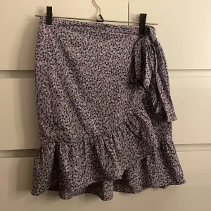 Mönstrad kjol från ONLY - Säljer en söt mönstrad kjol från ONLY i lila och svart. Kjolen har volangdetaljer och ett knytband i midjan. Storlek S, men man kan knyta den till den storleken man vill ha 💗💗