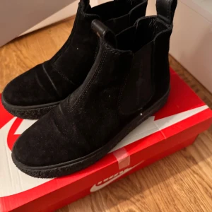 Svarta Canada snow skor - Snygga svarta Canada snow boots i mocka med elastiska paneler på sidorna för enkel på- och avtagning. Skorna har en robust sula med röd detalj och en liten dekorativ lönnlöv på framsidan. Perfekta för en stilren look. Pris kan diskuteras 