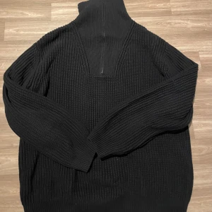 Svart stickad polotröja från Vailent - Säljer en svart stickad polotröja från Vailent. Tröjan har en hög krage och långa ärmar, perfekt för kyligare dagar. Den ribbade designen ger en stilren look.