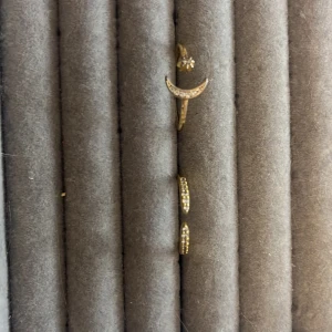 Guldfärgade ringar med stenar - Två justerbara guldfärgade ringar, en med en halvmåneformad design och små gnistrande stenar, och den andra med en enkel rad av stenar. Den med månen har själva guldet blivit dåligt men de är inget som syns när man har på sig den, den andra har inte defekter och ser ut som ny💗😻Dom kostar 50 st