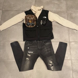 En 4-bundle med väst, byxor, stickad tröja och keps  - En 4-bundle där en The-north-face väst (ny pris 1600kr, st M), ett par jeans från Elias Rumelis (ny pris 1500, st W31), en stickad tröja från Jaggy (ny pris 699kr, st M) och en keps från New Era (ny pris 450kr, st 56,8 cm) ✅ Du tjärnar 2250kr.      Om du är sugen på att köpa något utav plaggen försig kolla profil✅