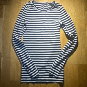 Randig långärmad tröja - Säljer en stilren randig tröja i svart och vit med långa ärmar. Perfekt för en avslappnad look. Tröjan har en klassisk rund halsringning och är gjord i ett mjukt material.