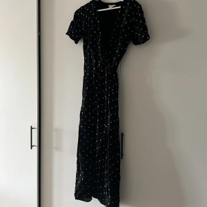 Svart långklänning med vita prickar - Säljer en superfin svart långklänning med vita prickar. Klänningen har korta ärmar och en knytning i midjan som ger en snygg passform. Perfekt för både fest och vardag! 🖤