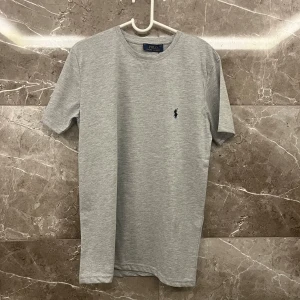 Grå t-shirt från Polo Ralph Lauren - Säljer en stilren grå t-shirt från Polo Ralph Lauren. Den har en klassisk passform med korta ärmar och är gjord i mjukt bomullsmaterial. På bröstet finns det ikoniska Polo Ralph Lauren-logotypen broderad i mörkblått. Perfekt för en avslappnad och snygg look!