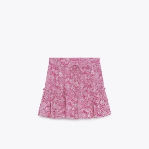 Rosa blommig kjol med volang - Säljer en superfin rosa kjol med blommigt mönster. Den har en söt volangdetalj och ett knytband i midjan. Kjolen är i nyskick och har en härlig passform. Den har shorts under. Oanvänd med lappen kvar. Storlek S