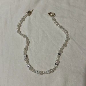 Pärlhalsband med bokstäver - Säljer ett snyggt Harry styles inspirerat pärlhalsband med vita pärlor och bokstavspärlor som stavar 'GOLDEN'. Halsbandet har en stilren design med en guldig låsning. liknar den som Harry har i golden musikvideon