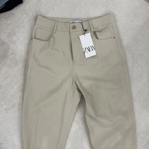 Beige byxor från Zara - Säljer ett par snygga beige byxor från Zara. De har en klassisk design med raka ben och en knappgylf. Perfekta för både vardag och fest!