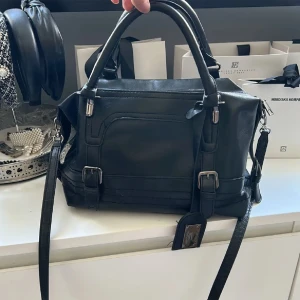 Svart handväska  - Supersnygg handväska som aldrig är använd. Ca 25cm bred. Axelband följer med och går att sätta dit och ta av💗