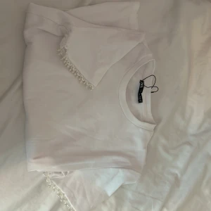 Vit t-shirt med spetsdetaljer från Zara - Säljer en superfin vit t-shirt från Zara. Den har korta ärmar och en söt spetsdetalj vid ärmsluten som ger en extra touch. Perfekt för både vardag och festliga tillfällen!