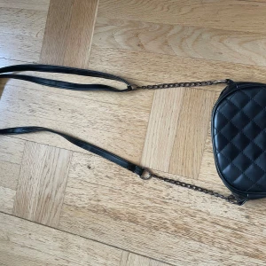 Svart quiltad axelväska - Säljer en snygg svart axelväska med quiltat mönster. Väskan har en kedja som axelrem och en praktisk dragkedja upptill. Skriv gärna om ni har frågor 💕