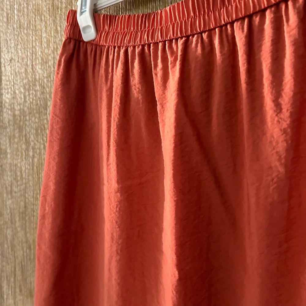 Säljer en superfin orange långkjol. Den är enkel och stilren med en elastisk midja som gör den bekväm att bära. Perfekt för sommaren eller våren! Kjolen är i ett lätt och luftigt material, vilket gör den idealisk för varma dagar. Passar både till vardags och fest. Den har slitsar på båda sidorna och fickor. . Hameet.